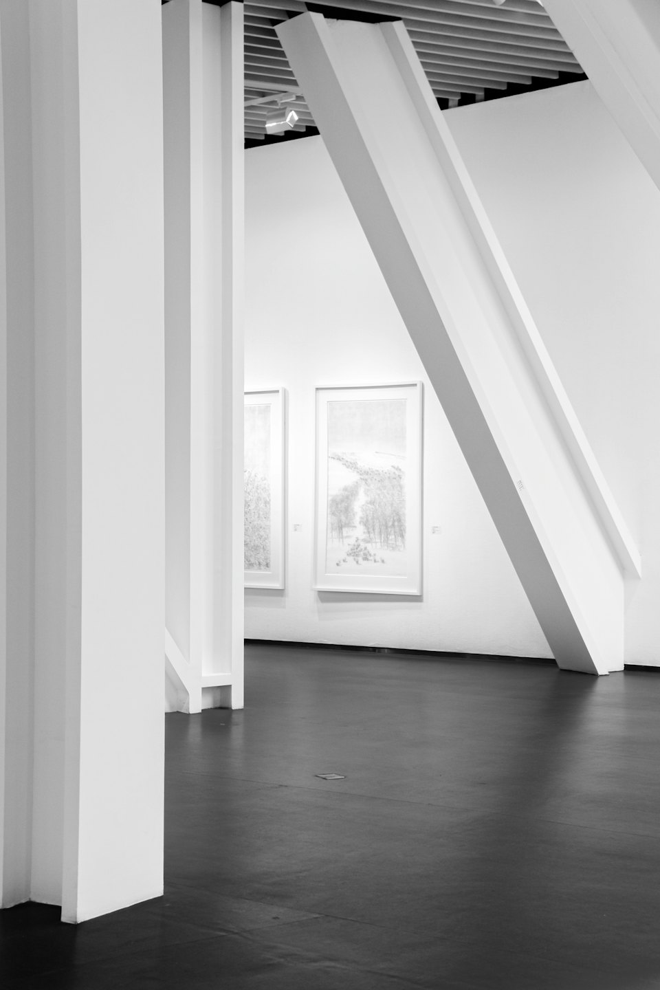Dwa obrazy wiszą na białej ścianie w minimalistycznej galerii.