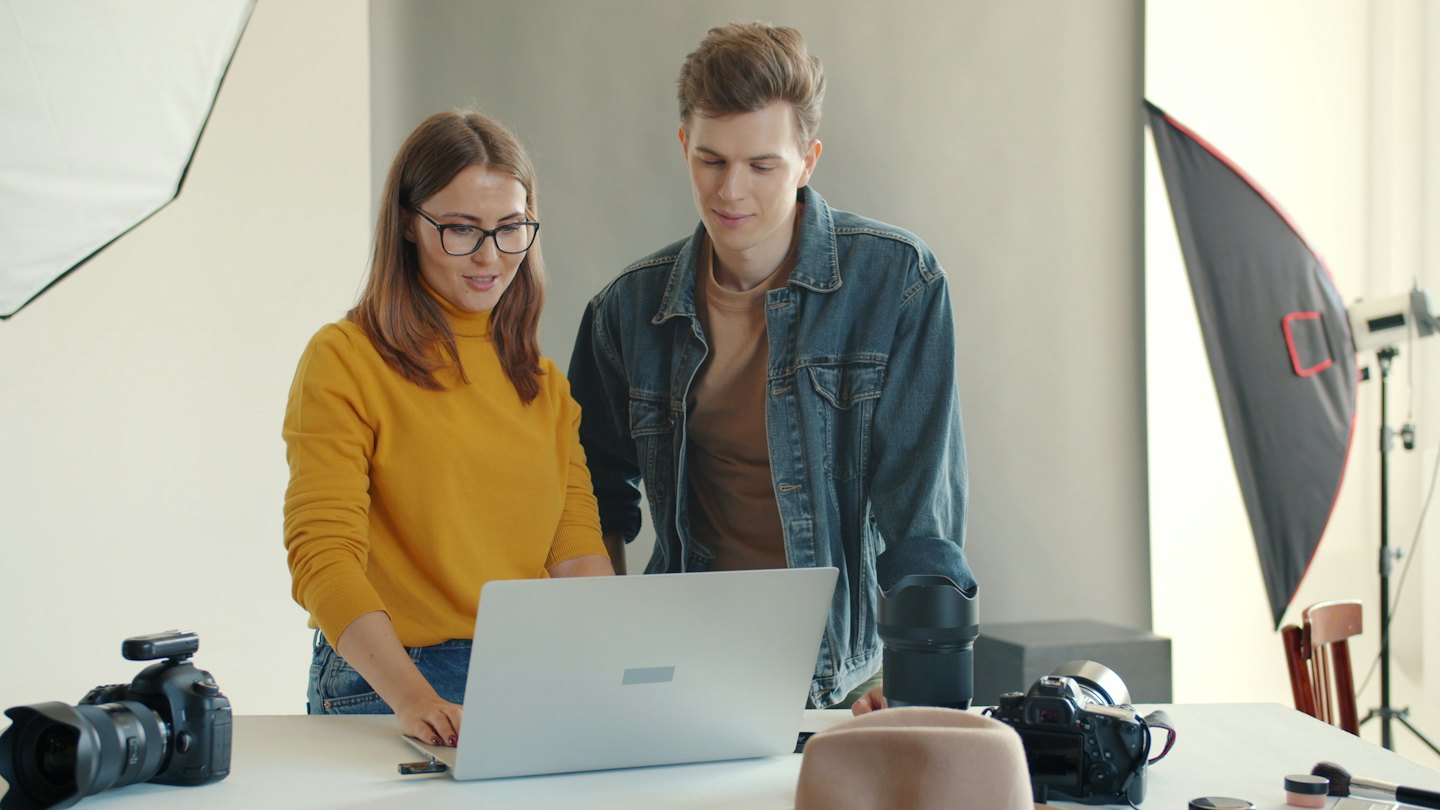 Dwóch fotografów przegląda laptopa przy stole w studiu.
